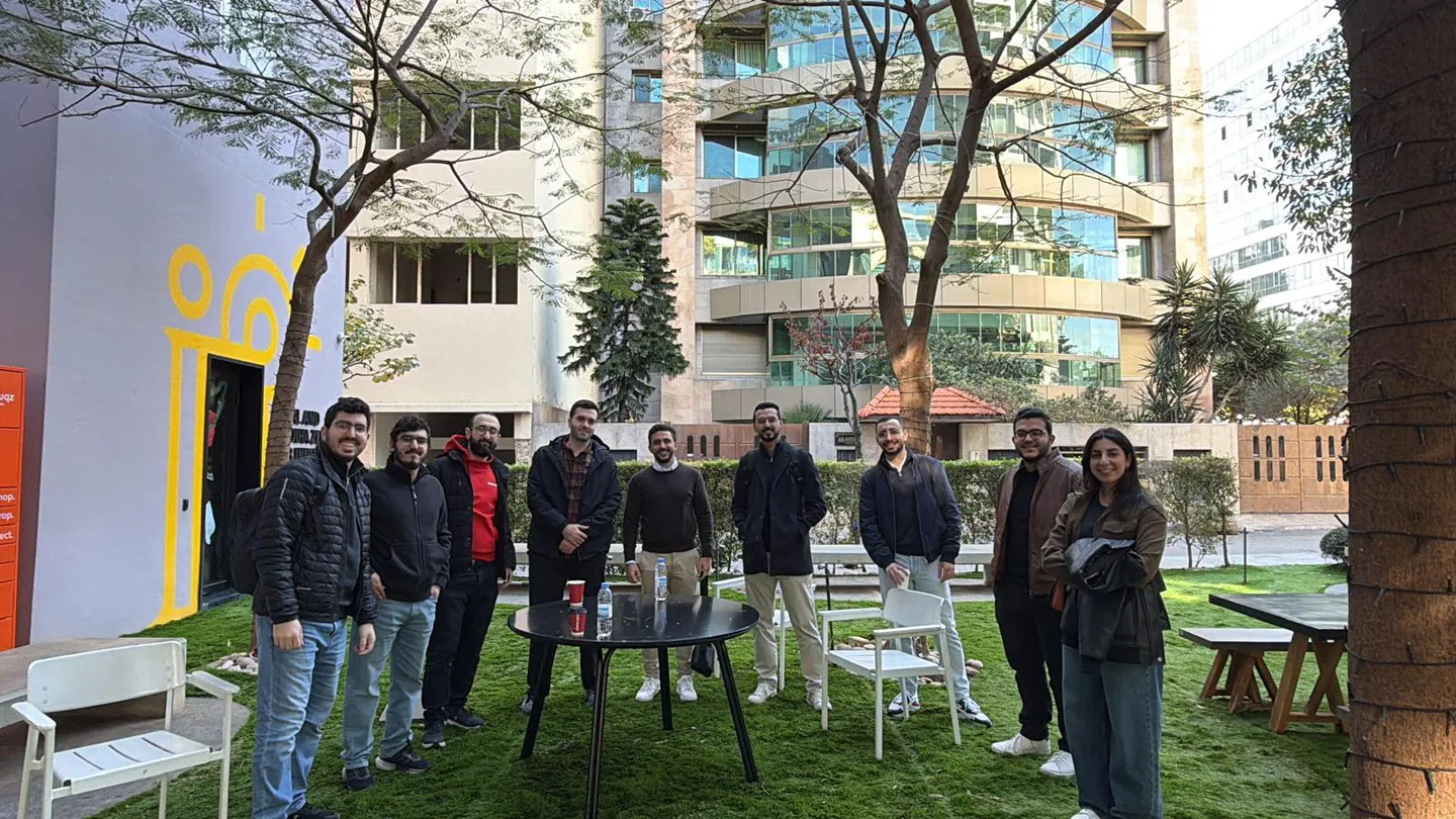 Nine attendees stand around a table in the tree-lined courtyard at Beirut Digital District