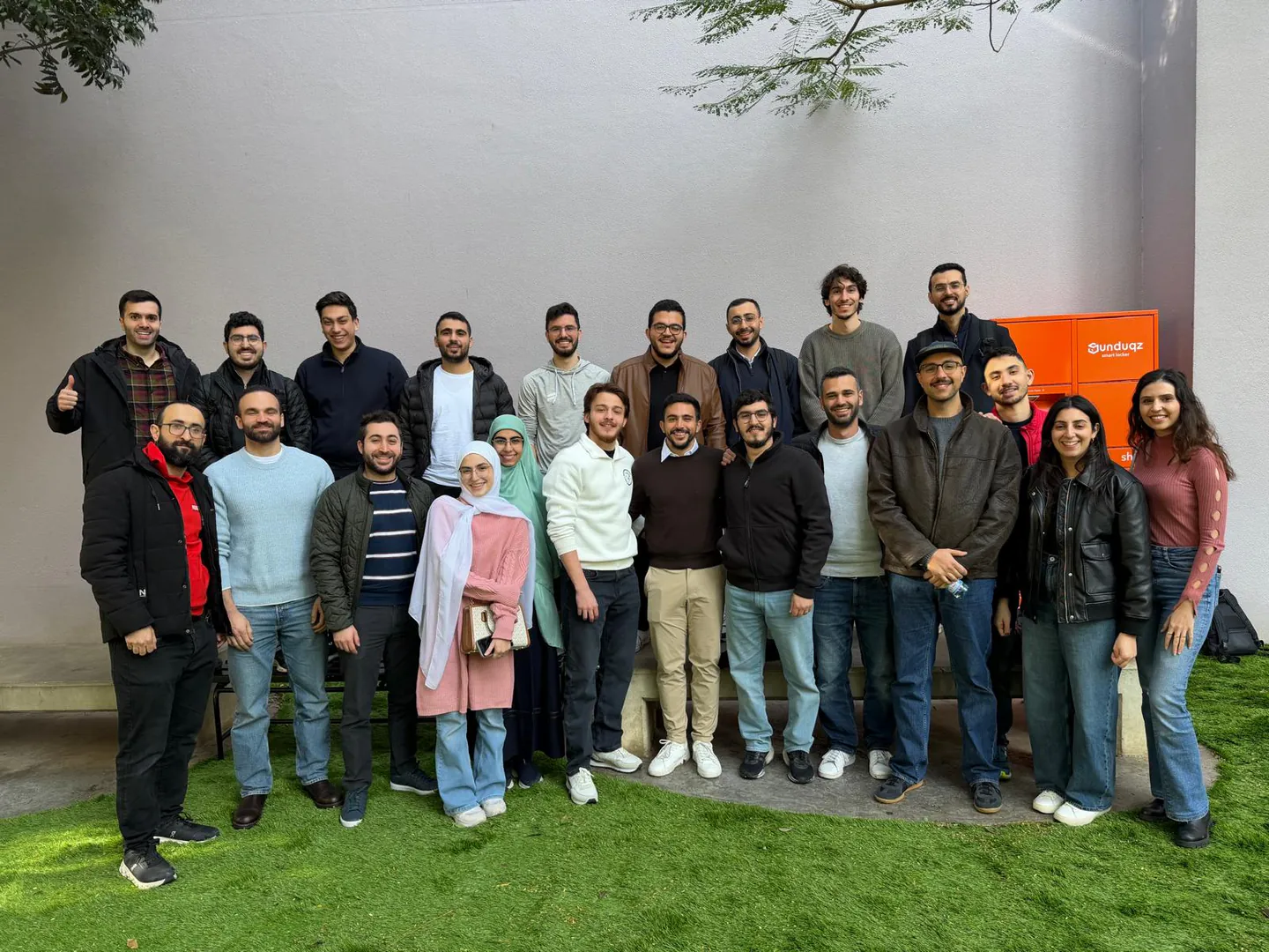 A large group of smiling attendees pose in two rows in the Beirut Digital District courtyard